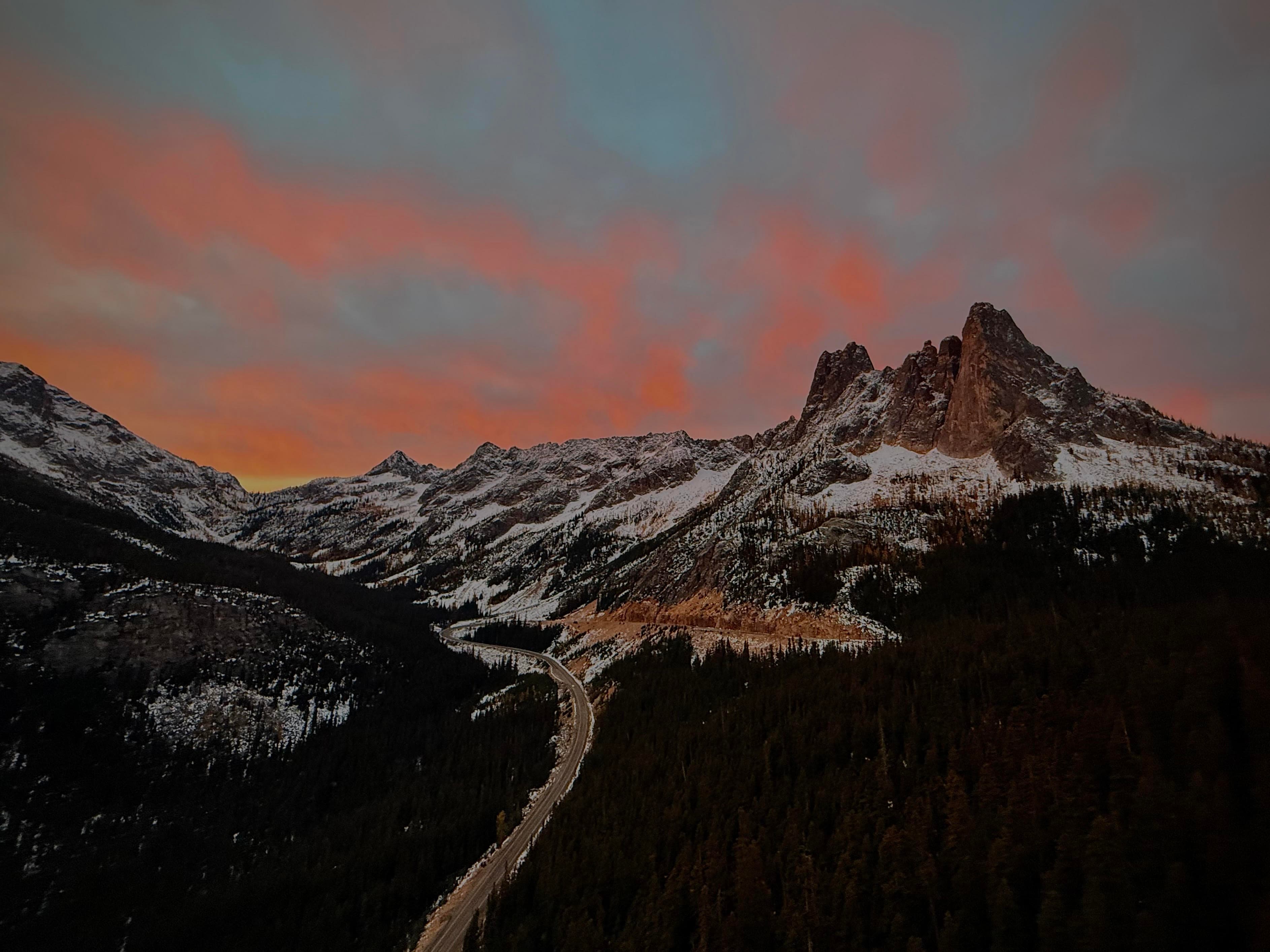 Sunset over snow-dusted peaks above a winding mountain road